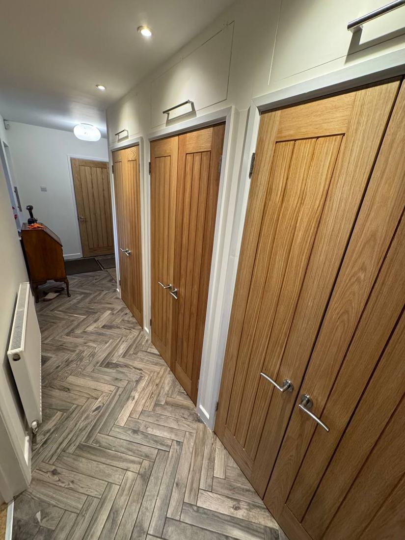 Row of oak cottage doors along a hallway with grey herringbone flooring